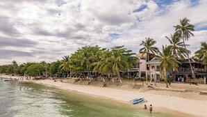 Une plage bordée de palmiers, un bateau et un bâtiment doté d’un balcon.