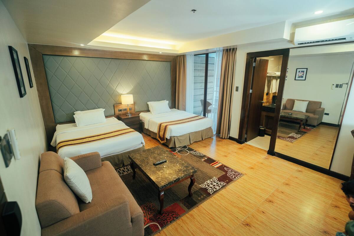 Habitación de hotel con dos camas, un sofá, una mesita de centro y un espejo.