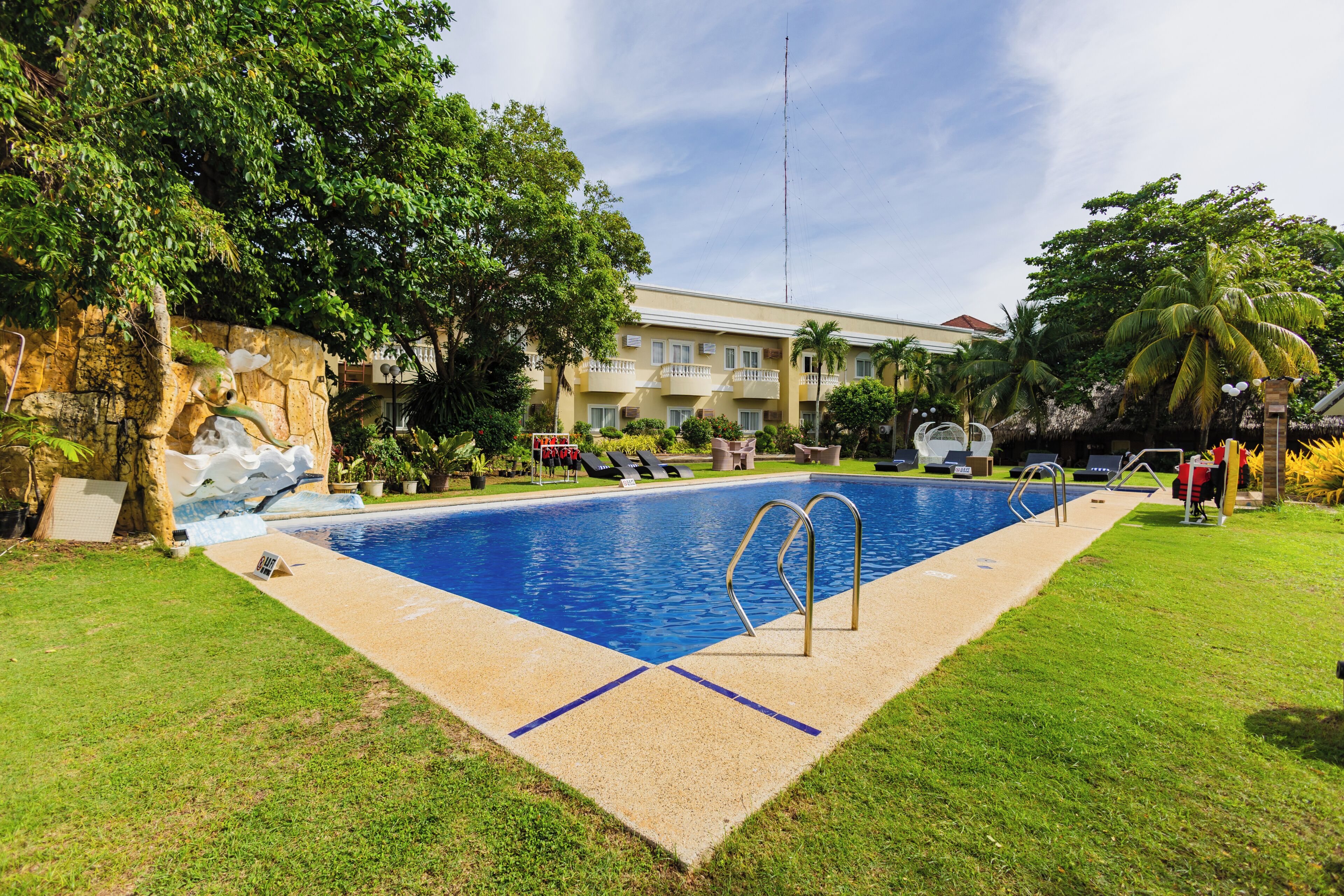 A swimming pool with a stone wall, grass, and a building in the background.