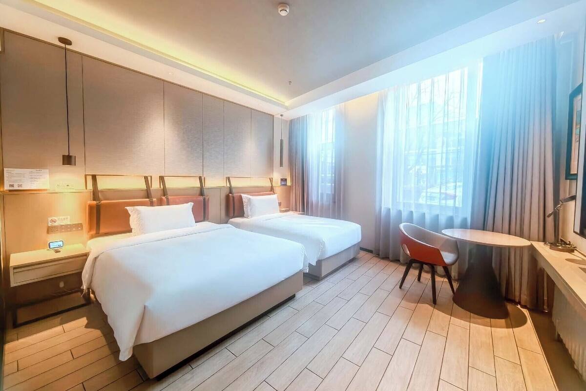 A hotel room with two beds, a desk, a chair, and a window with curtains.