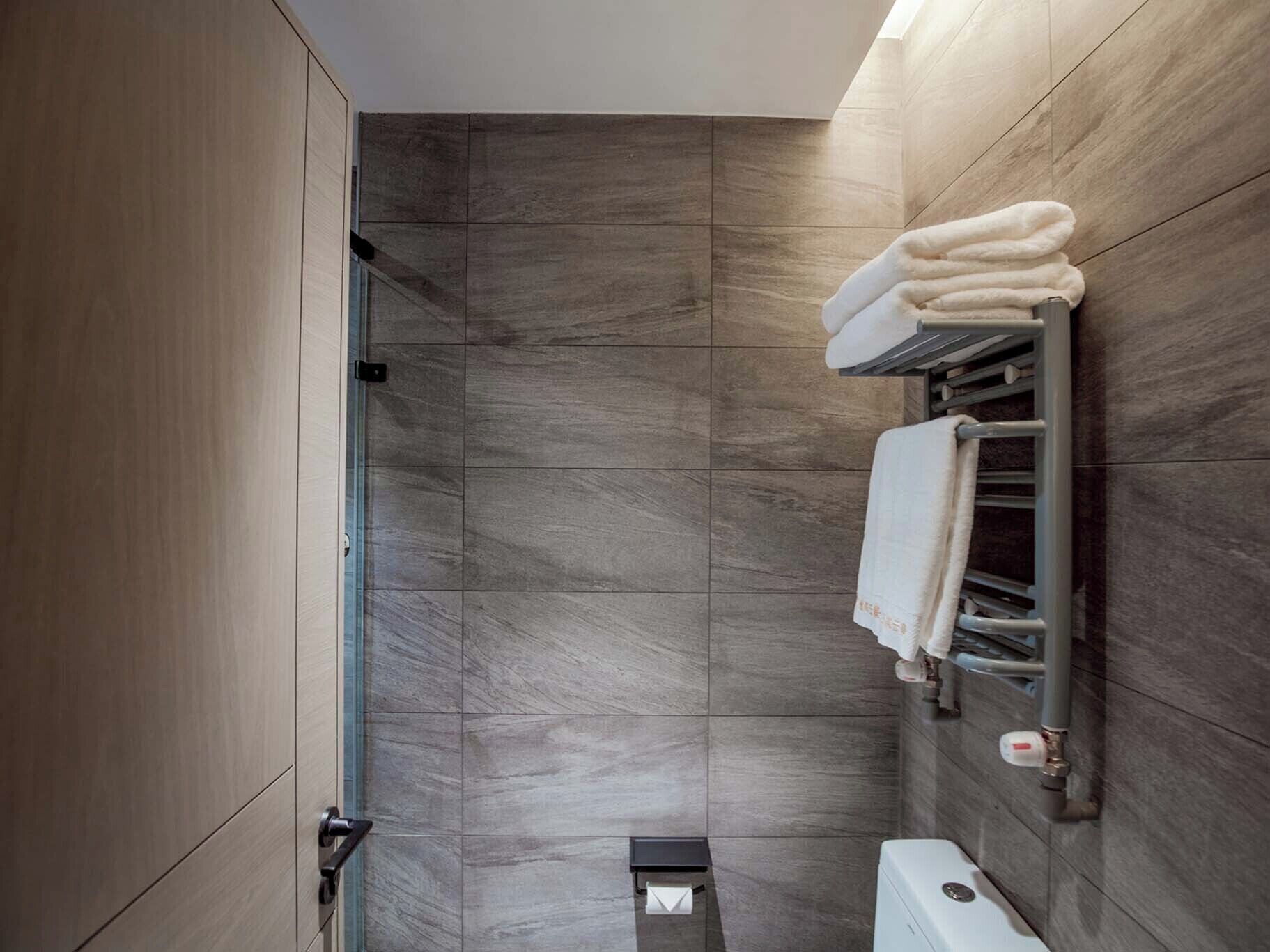 A modern bathroom with a walk-in shower, a toilet, and a towel rack.