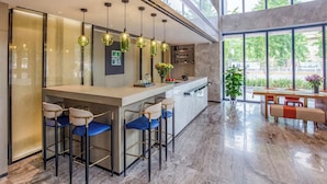 Uma área de bar moderna com bancada de mármore, banquetas e iluminação pendente.