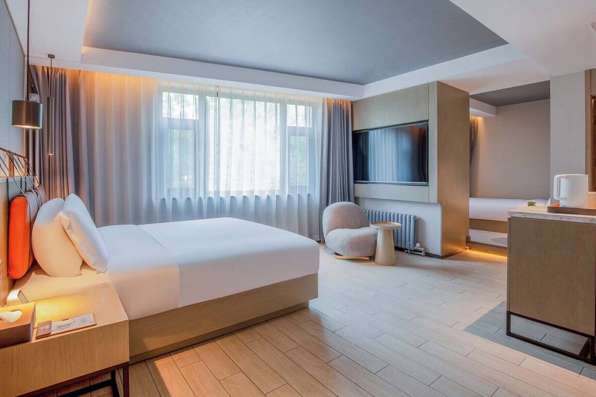A modern hotel room with a large bed, a seating area with a chair and a table, a television, and a small desk.