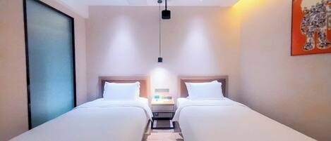 Habitación de hotel con dos camas individuales, una mesita de noche, una lámpara en el techo y un cuadro en la pared.