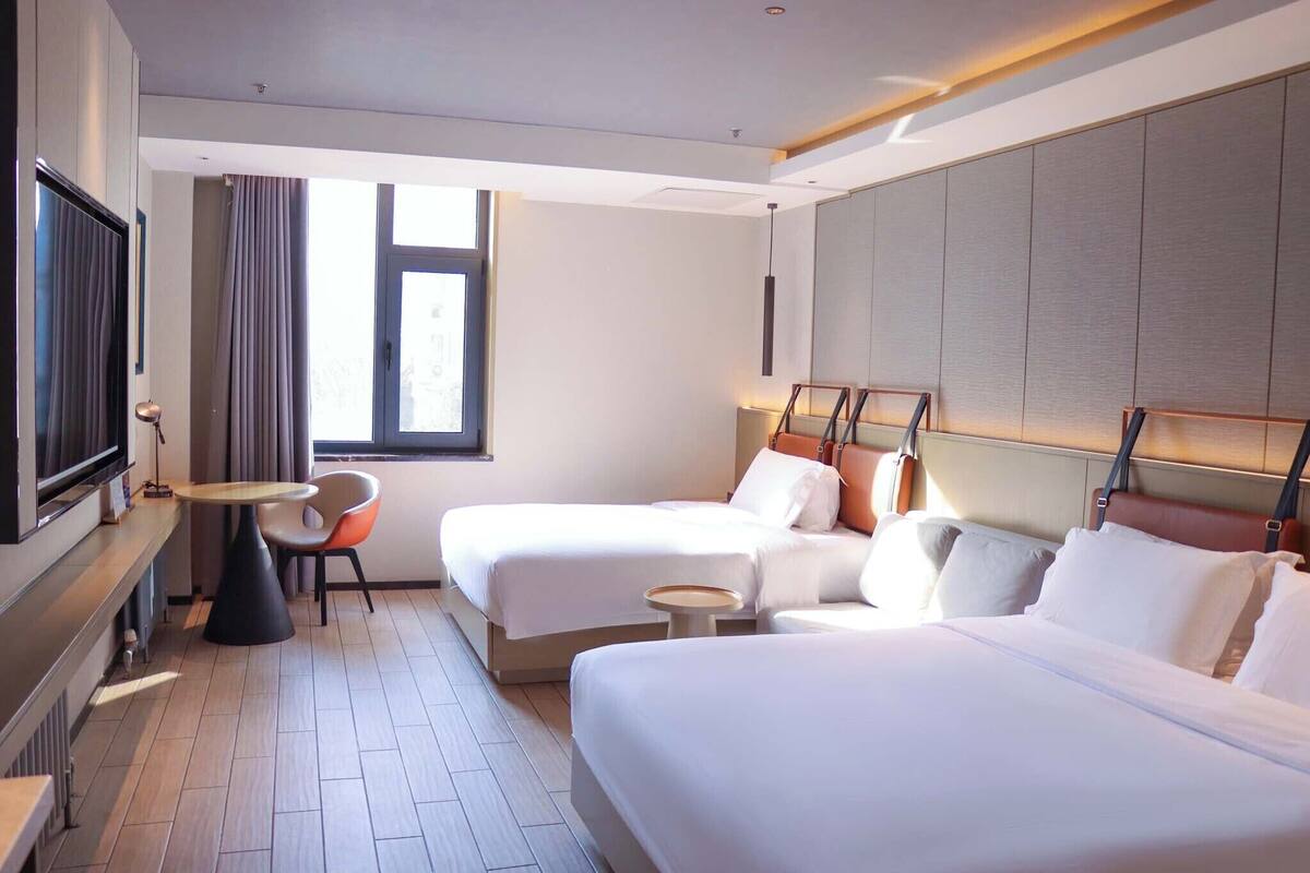 A hotel room with two beds, a TV, a small table, and a chair.