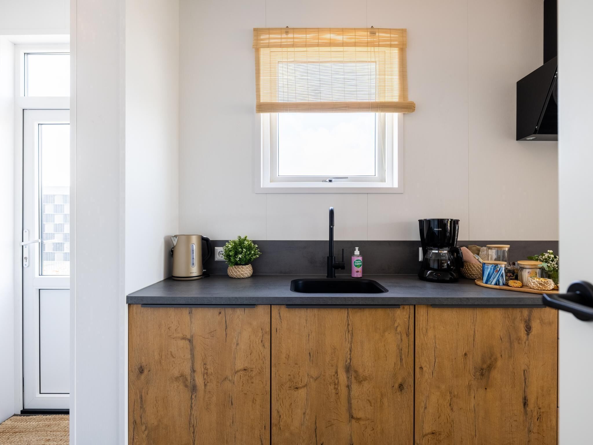A kitchen with a wooden countertop, a coffee maker, a kettle, and a window with blinds.