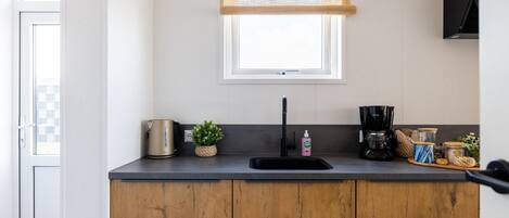 A kitchen with a wooden countertop, a coffee maker, a kettle, and a window with blinds.