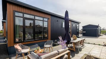 A modern building with large windows, outdoor seating, and a garden area.