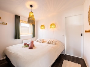 Een keurig opgemaakt slaapkamer met een groot bed, twee wandlampen, een raam met gordijnen en een deur.
