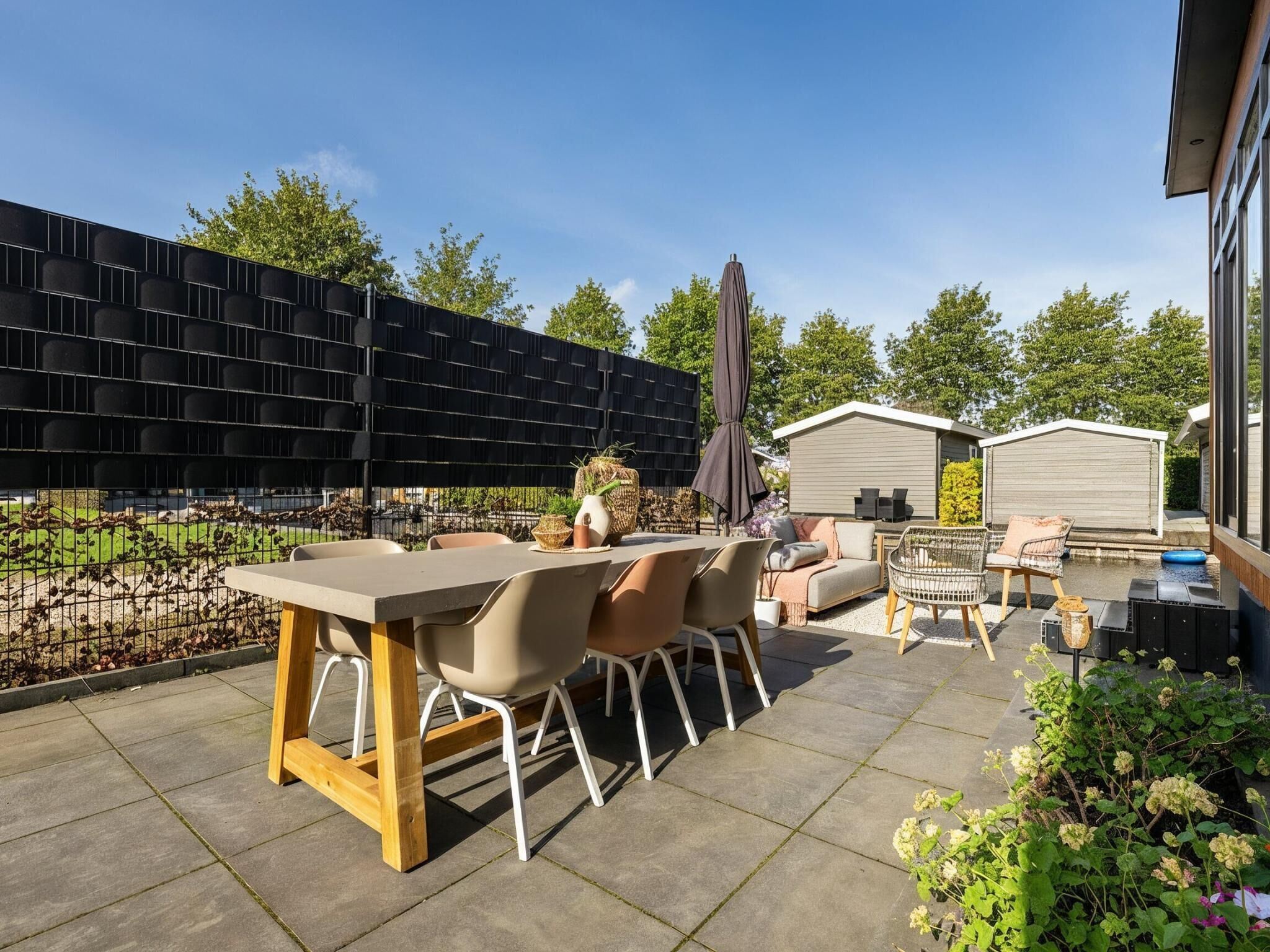 Un patio al aire libre con una mesa y sillas, una zona de estar cubierta y un jardín.