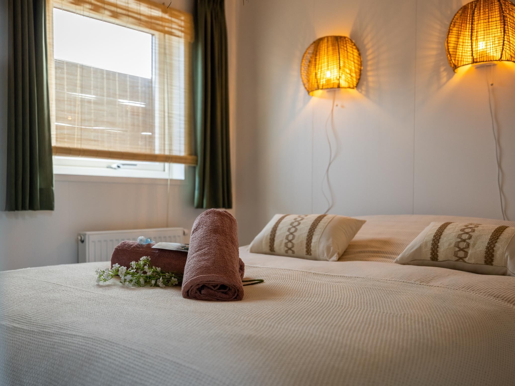 Una habitación de hotel con cama, ventana con cortinas y dos lámparas fijadas a la pared.