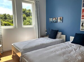 A bedroom with two beds, a window with curtains, a bedside table with a lamp, and artwork on the wall. - Villa Lastavica - swimming pool - large garden - walking distance to the beach (Vis)