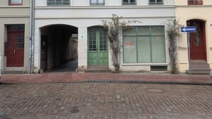A two-story building with a ground-level entrance, a visible sign, and a brick-paved street in front. - Altstadt vacation apartment first floor (Wismar)