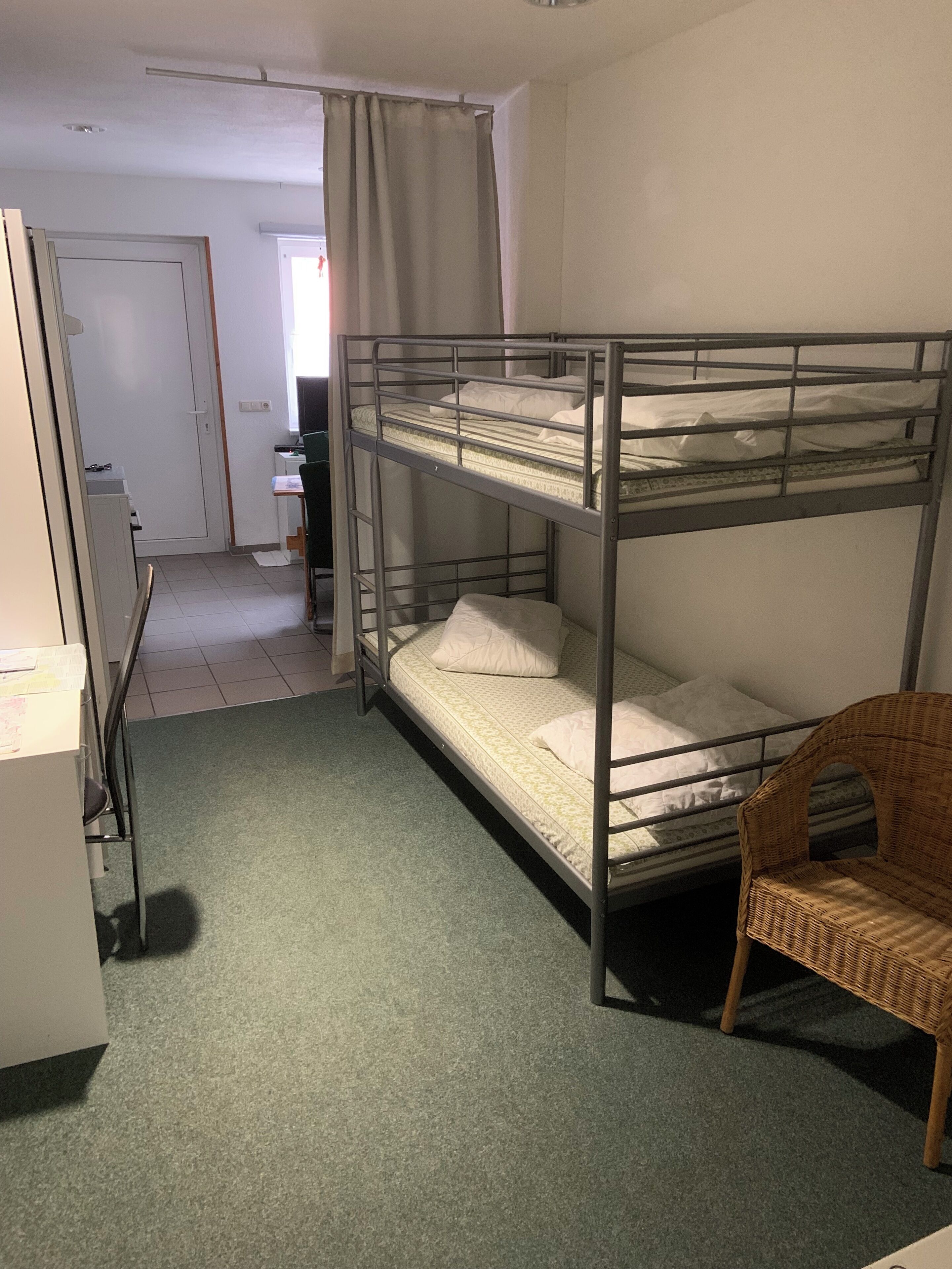A bunk bed room with a desk, chair, and a wicker chair.
