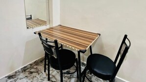 Ein kleiner Essbereich mit einem Holztisch, zwei schwarzen Stühlen, einem Boden mit Marmoroptik und einem Spiegel an der Wand.