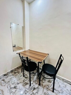 Un pequeño comedor con una mesa de madera y dos sillas negras, piso con diseño de mármol y un espejo en la pared.