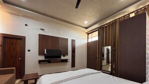 A bedroom with a bed, a TV, a wooden wardrobe, a mirror, and a door. - Mansarovar Villa (Pindra)