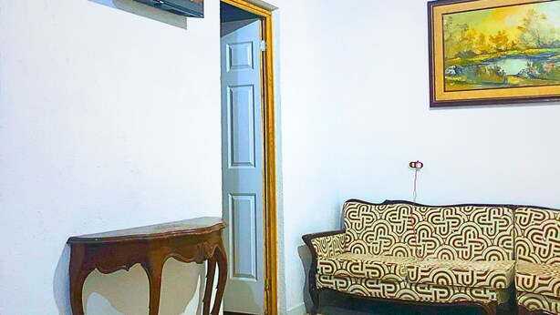 Una habitación con techo de madera, un televisor montado en la pared, una puerta, un sofá estampado y una pequeña mesa.