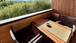 Een houten terras met een tafel en stoelen, uitkijkend op een groen landschap.