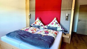 Una cama con estructura de madera, cabecera roja y almohadas estampadas con motivos florales.