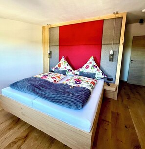 Ein Bett mit Holzrahmen, einem roten Kopfteil und Kissen mit Blumenmuster.