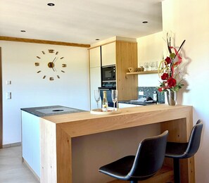 Eine moderne Küche mit einer Holztresenplatte, zwei schwarzen Stühlen, einer Uhr und einer Vase mit Blumen.