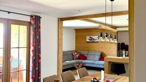 Un comedor con una mesa de madera, sillas, un soporte para código QR y un sofá al fondo.