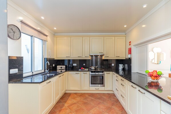 A modern kitchen with white cabinets, black countertops, and a tiled floor.