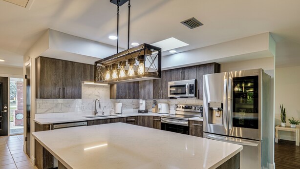 Une cuisine moderne dotée d’un grand îlot central, d’appareils électroménagers en acier inoxydable et d’un design de style champêtre.