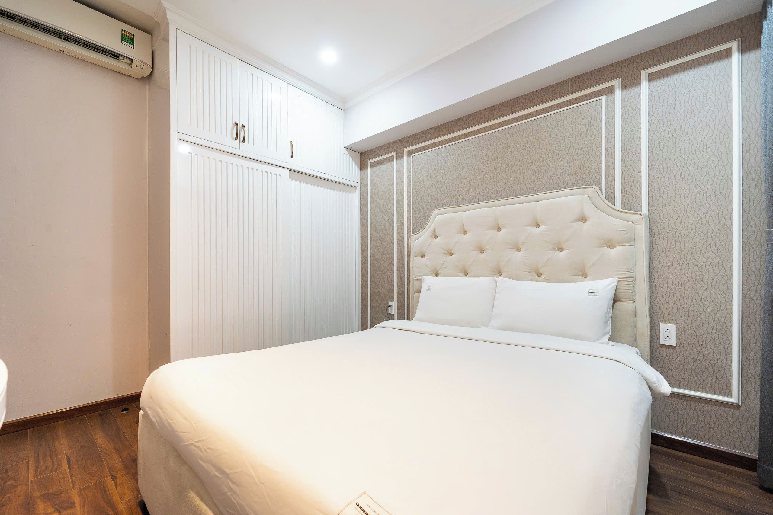 A bedroom with a large bed, white wardrobe, and a wall-mounted air conditioner.