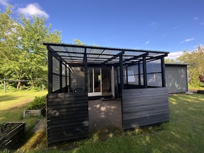 A small, single-story structure with a covered patio area, a sliding glass door, and a visible interior space. - Cozy holiday home only 700 m from the water (Gilleleje)
