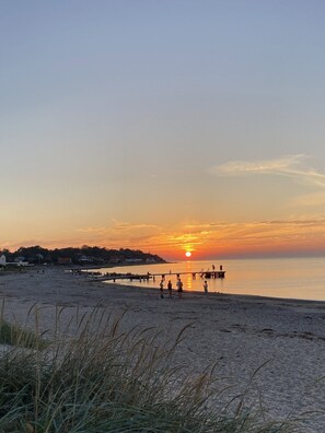 A beach scene with a sunset, a pier, and people walking. - Cozy holiday home only 700 m from the water (Gilleleje)