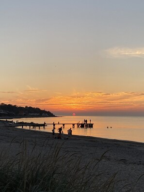 Cena de praia com pessoas, um píer e um pôr do sol.