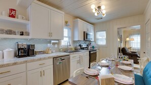 A modern kitchen with white cabinets, stainless steel appliances, and a dining area with a wooden table set for four. - 1 Mile to UA Campus: Walkable Midtown Getaway (Tuscaloosa)