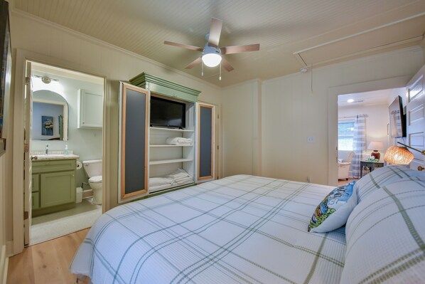 Ein Schlafzimmer mit Bett, Deckenventilator, Fernseher und begehbarer Kleiderschrank.