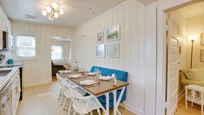 A dining area with a wooden table set for four, white chairs, a blue sofa, and a kitchen in the background. - 1 Mile to UA Campus: Walkable Midtown Getaway (Tuscaloosa)