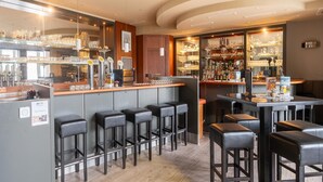Zona de bar con taburetes, estanterías llenas de vasos y una barra con caja registradora.