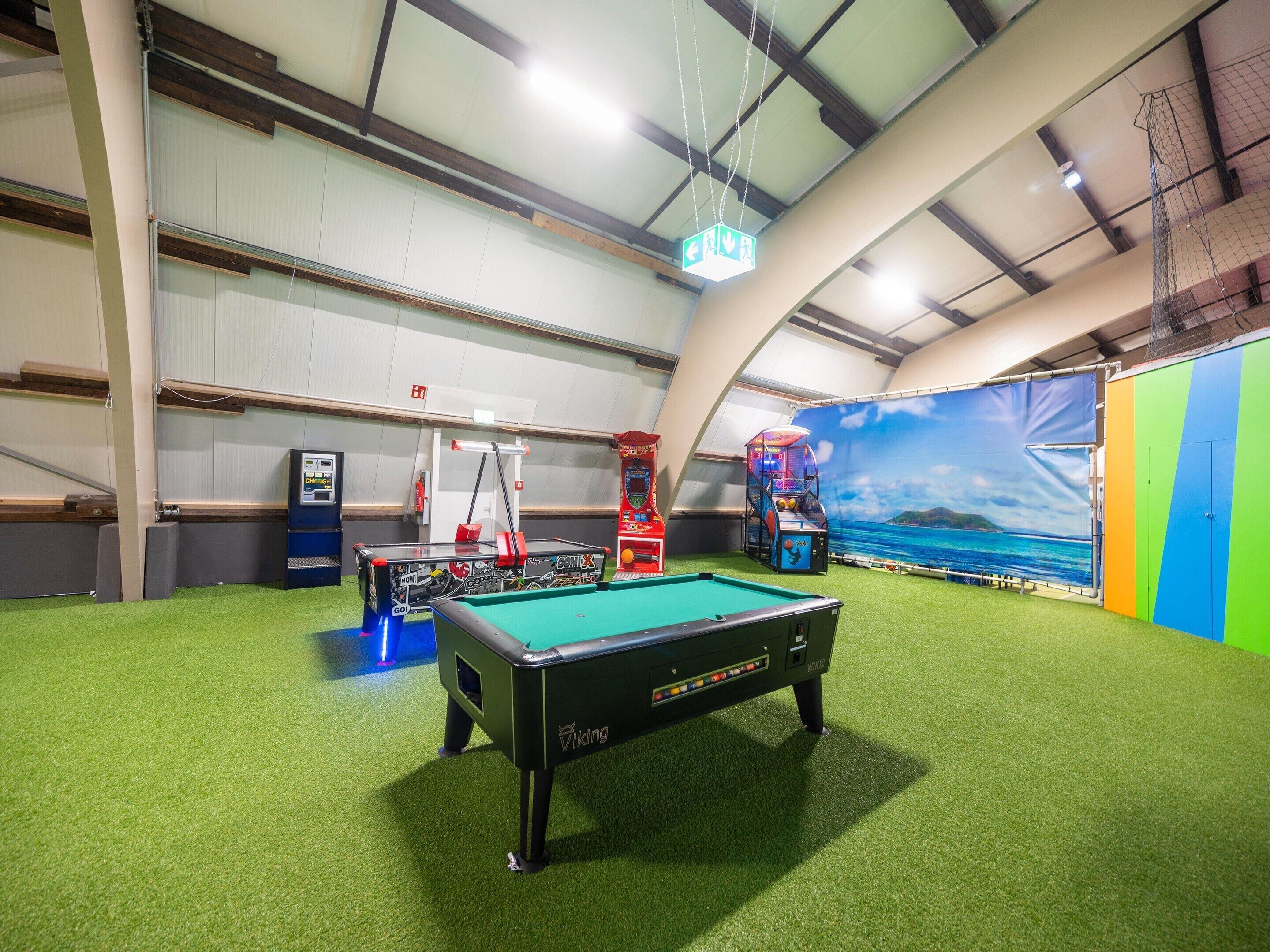 Un espace de loisirs intérieur comprenant une table de billard, des jeux d’arcade et un mur d’escalade.