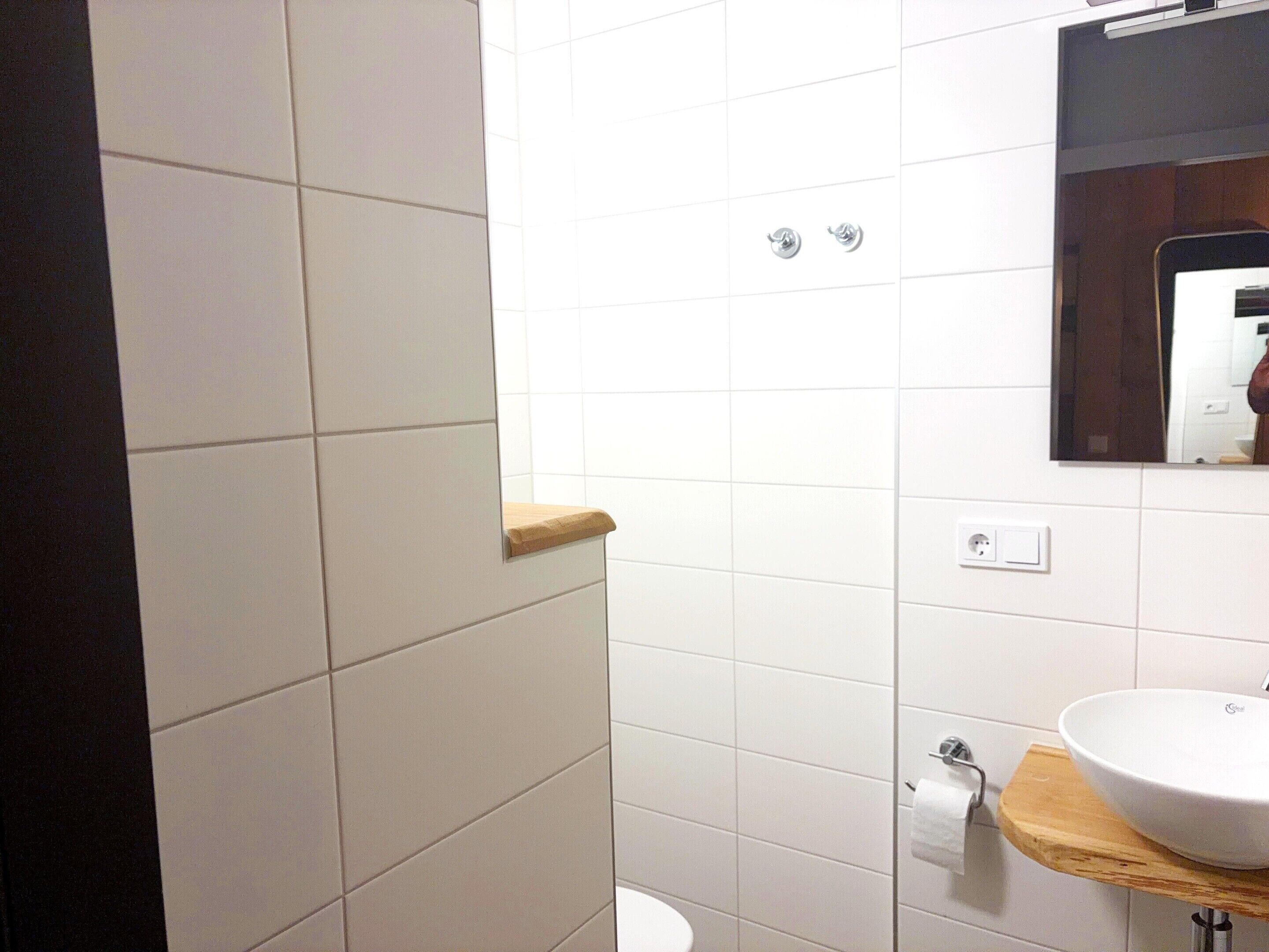 Une salle de bain avec des carreaux blancs, un plan de toilette en bois, un lavabo, des toilettes et un miroir.