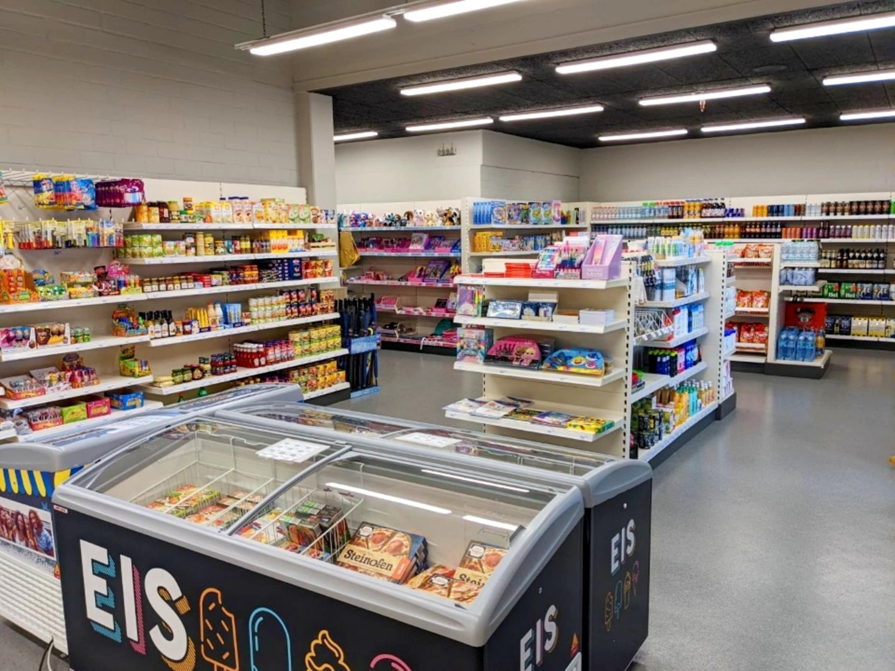 Interieur van een supermarkt met schappen vol diverse producten, een vriesvak en een koeling.