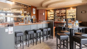 A bar area with stools, a counter, and shelves with glasses and bottles.