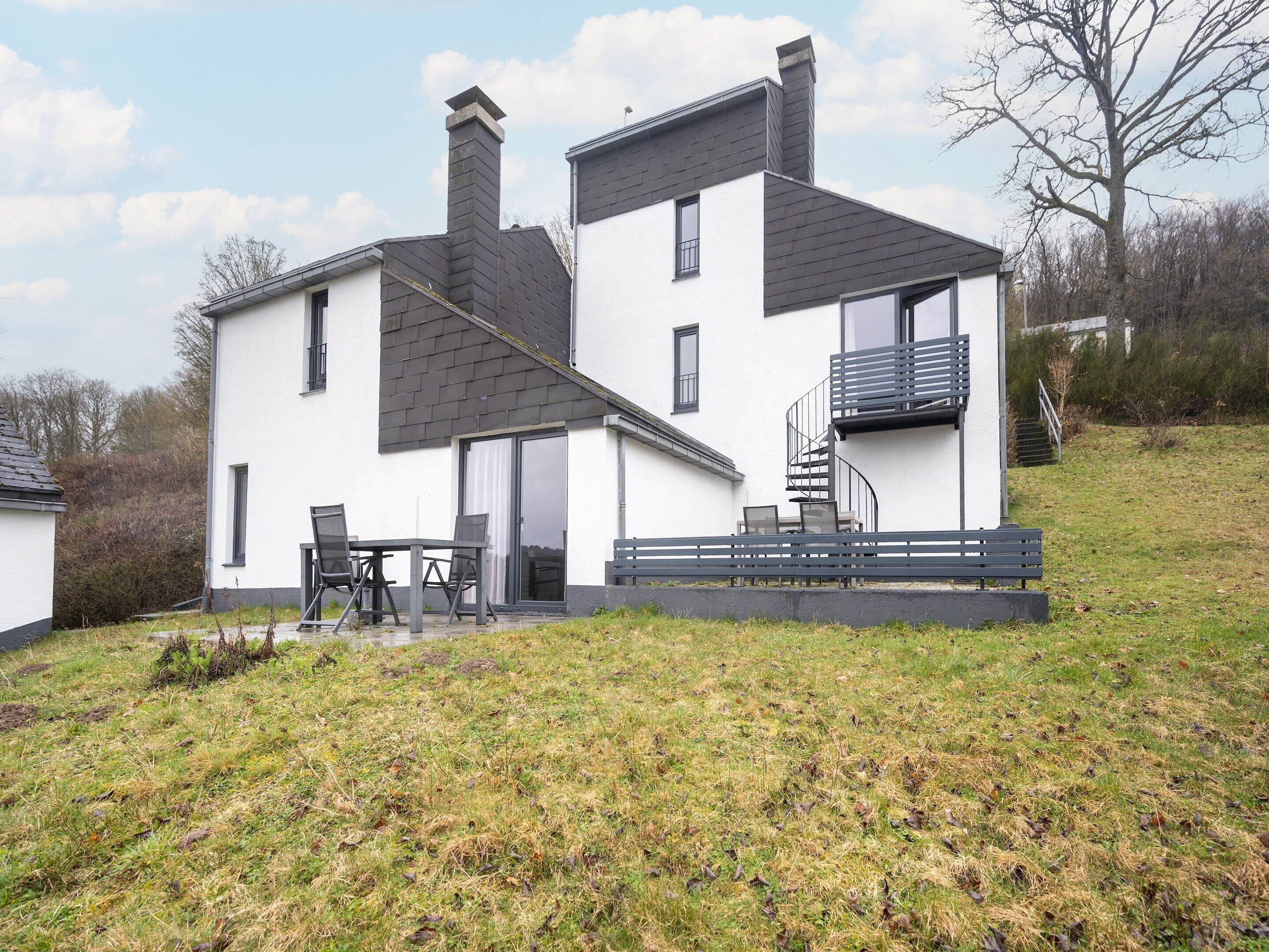 Een modern huis met twee verdiepingen, een balkon, een terras met tuinmeubilair en een gazon.