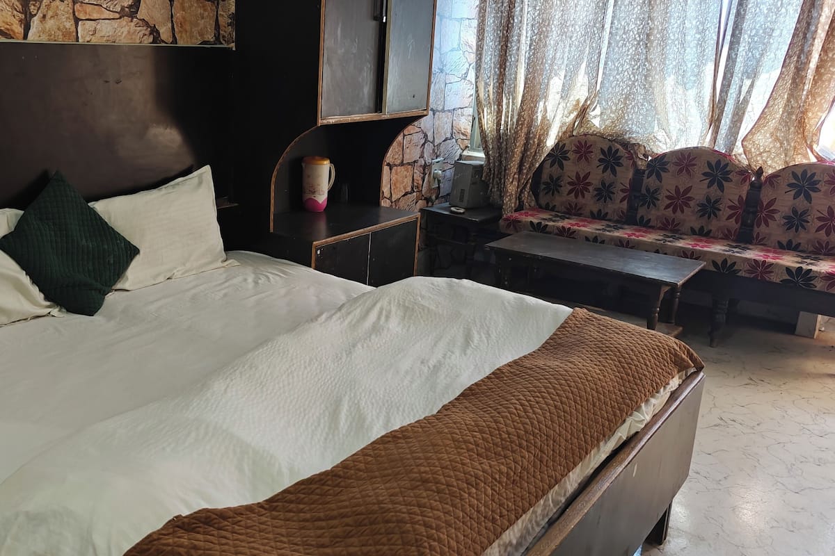 A hotel room with a large bed, a sofa, a small table, and a stone wall.