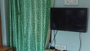 Un dormitorio con una cama, un televisor montado en la pared, un enchufe y un estante de madera.
