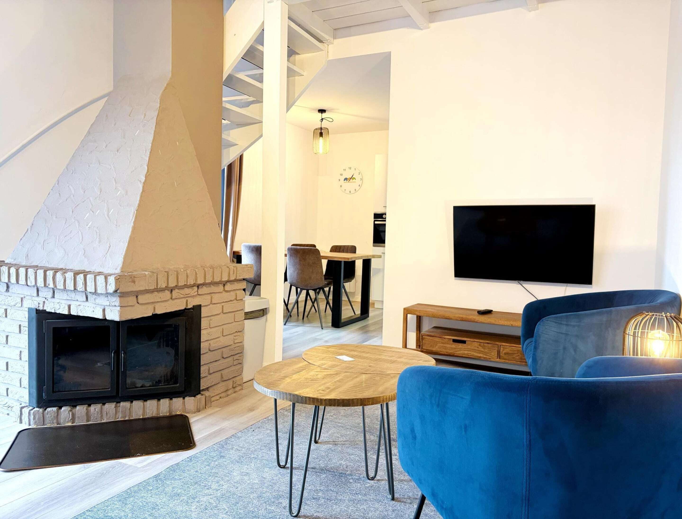 Una sala de estar moderna con chimenea, televisor montado en la pared y un sofá azul.