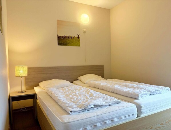 Une chambre d’hôtel avec deux lits, une table de chevet, une lampe et un tableau accroché au mur.