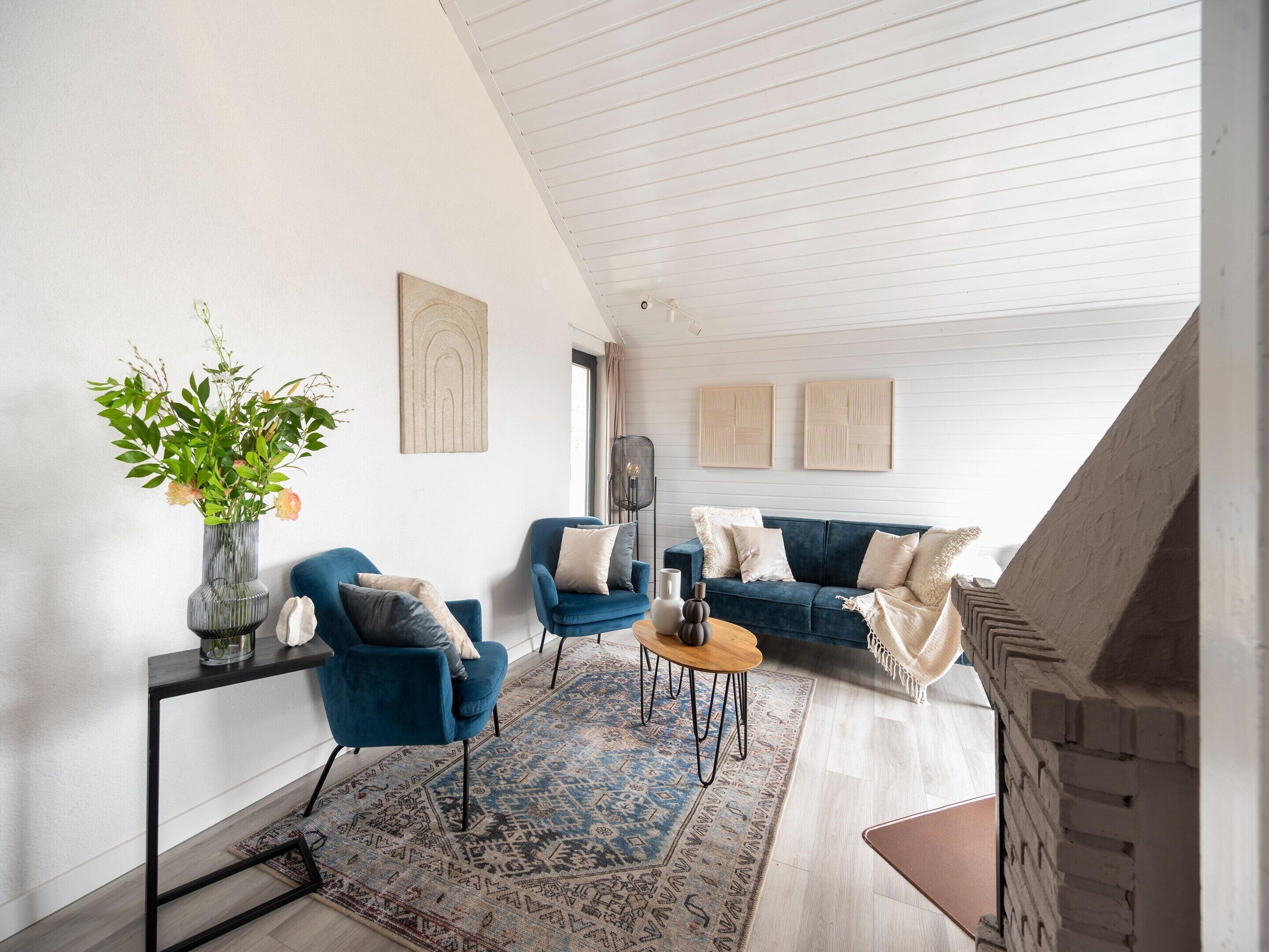 Uma sala de estar moderna com um sofá azul, uma poltrona azul, uma mesa de centro, um tapete estampado e um vaso com flores.