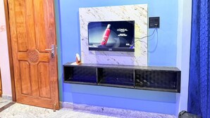 A room with a wooden door marked '103', a TV mounted on a marble wall, and a black entertainment unit below. - Om Sai Ram Paying Guest House (Varanasi)