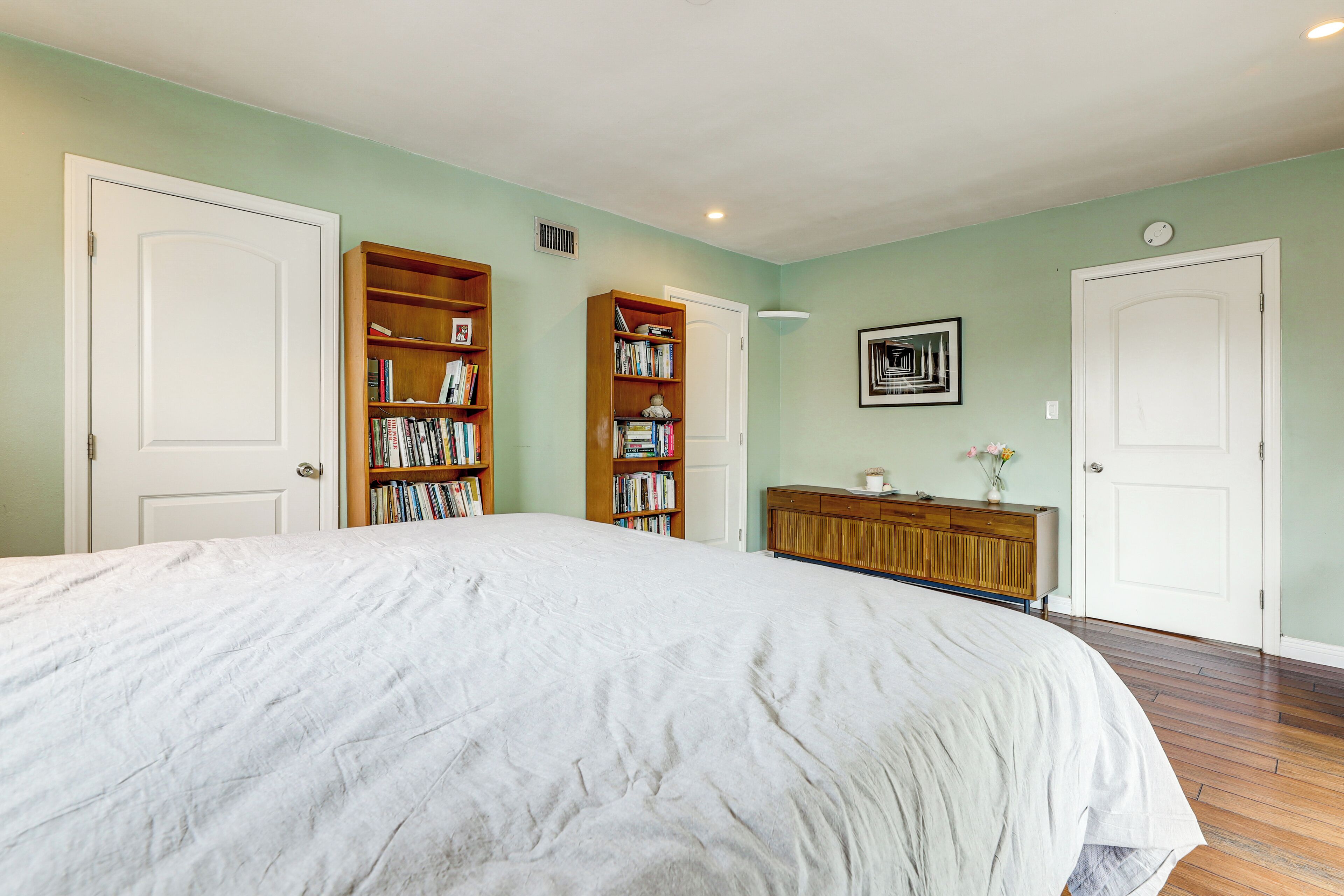 A bedroom with a large bed, two wooden bookshelves, a wooden dresser, and a white door.