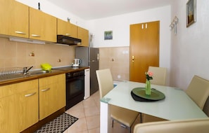 A compact kitchen with wooden cabinets, a built-in oven, a coffee maker, and a dining table with chairs. - Stunning apartment in Brela with WiFi (Brela)